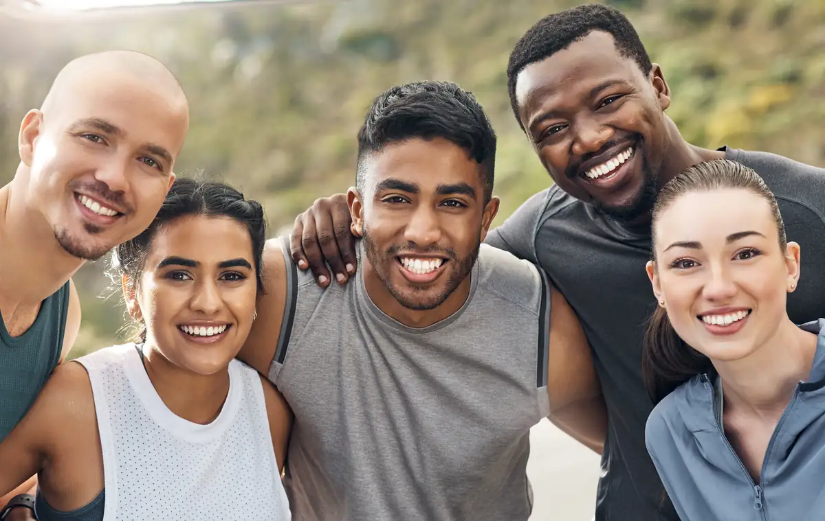 Five friends in athletic wear smiling together after an outdoor workout