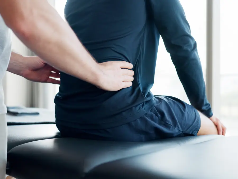 Chiropractor examining the lower back of a man seated on a treatment table