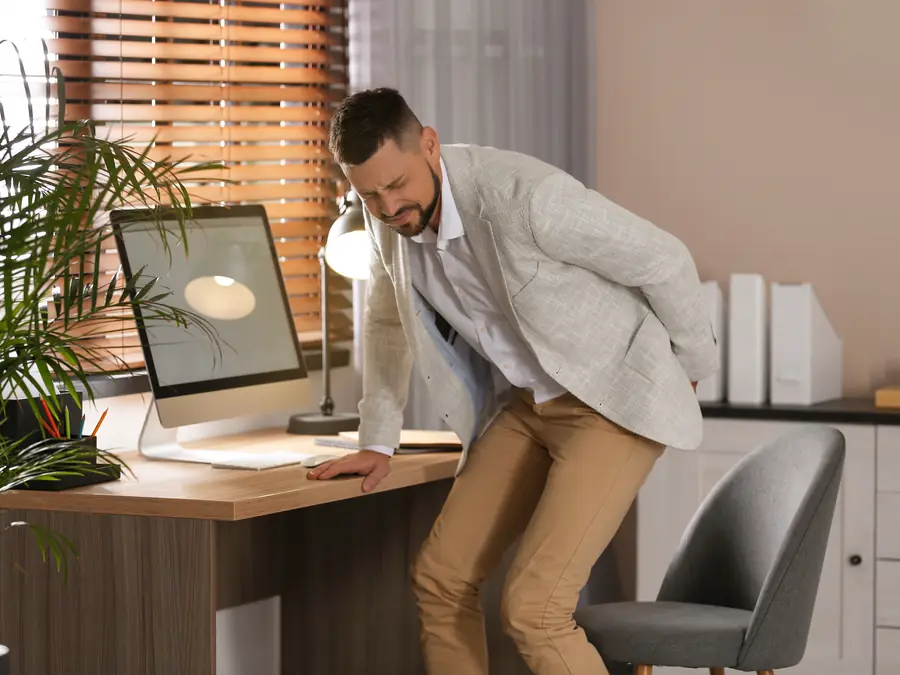 Man at work bracing on his desk with sudden lower back pain