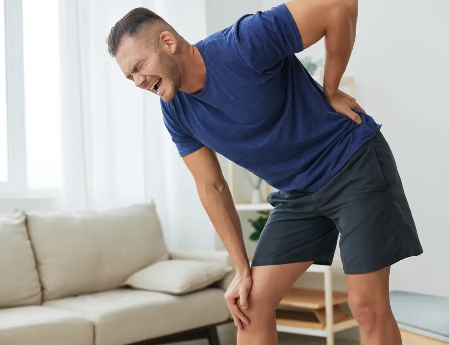 Man bending forward holding his lower back and knee from sciatica pain