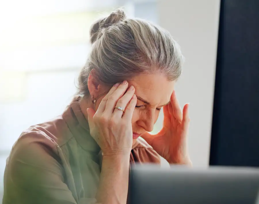 Woman at her desk pressing her temples during a tension headache
